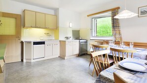 Une cuisine moderne avec des meubles blancs, une table à manger avec des chaises et une fenêtre donnant sur un paysage verdoyant.