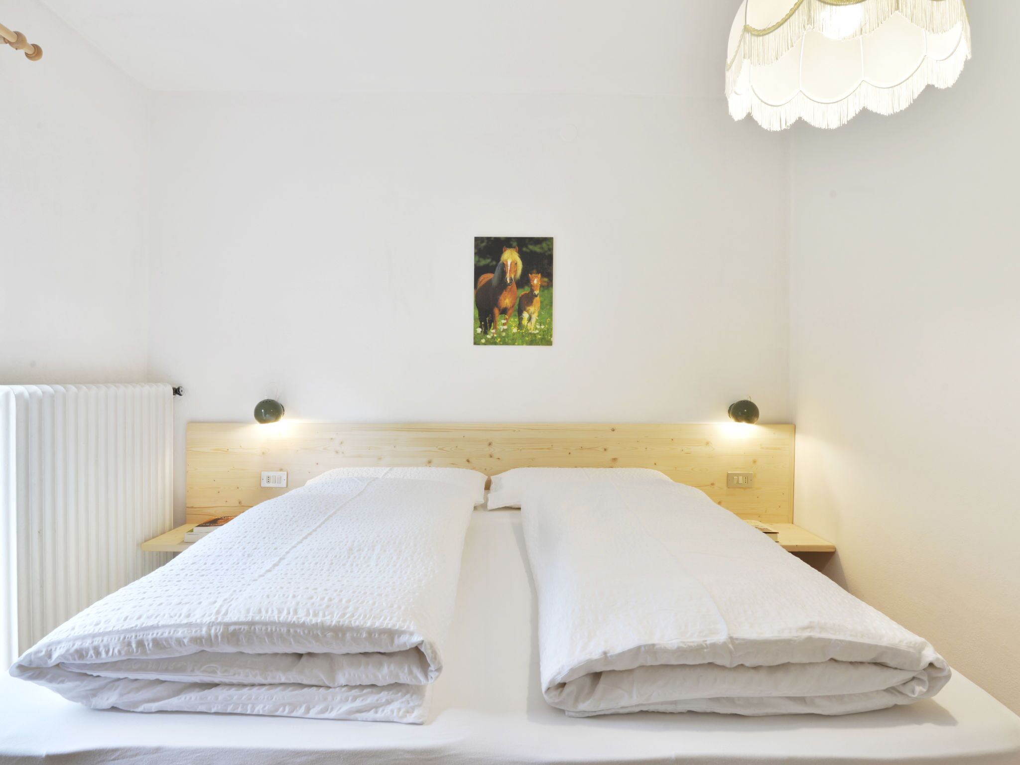 Ein ordentlich bezogenes Bett mit weißer Bettwäsche, einem Holz-Kopfteil und einem kleinen Bild von Pferden an der Wand.