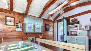 A rustic wooden cabin interior with a dining table, benches, a kitchen area with vintage appliances, and a large window with curtains. - Apartment Viliam by Interhome (Rovinj)