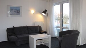 A modern living room with a grey sofa, a white coffee table, and a grey armchair. There is a framed picture on the wall, a floor lamp, and a window with curtains. - Apartment Duhnen by Interhome (Cuxhaven)