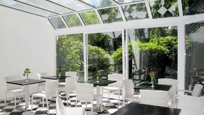 A sunlit patio with checkered flooring, white wicker furniture, and large glass windows offering views of greenery. - Apartment Duhnen by Interhome (Cuxhaven)