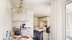 A compact hotel room with a dining area, kitchenette, and a large window with curtains. - Apartment Duhnen by Interhome (Cuxhaven)