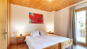 Una camera da letto con un letto in legno, due comodini, un tavolino da notte, una finestra con tende e un quadro appeso al muro.