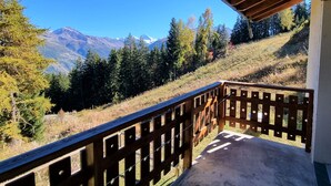 Un balcone con ringhiera in legno che si affaccia su un paesaggio montuoso con alberi e cielo sereno.