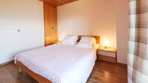 A bedroom with a wooden ceiling, a large bed with white bedding, two bedside lamps, and a wooden nightstand. - Edelweiss by Interhome (Thyon-Les Collons)
