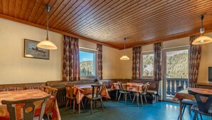 Un comedor con mesas y bancos de madera, ventanas amplias con cortinas y lámparas colgantes.