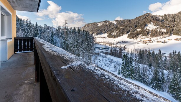 Un balcón de madera con vistas a un paisaje montañoso nevado y un cielo despejado.