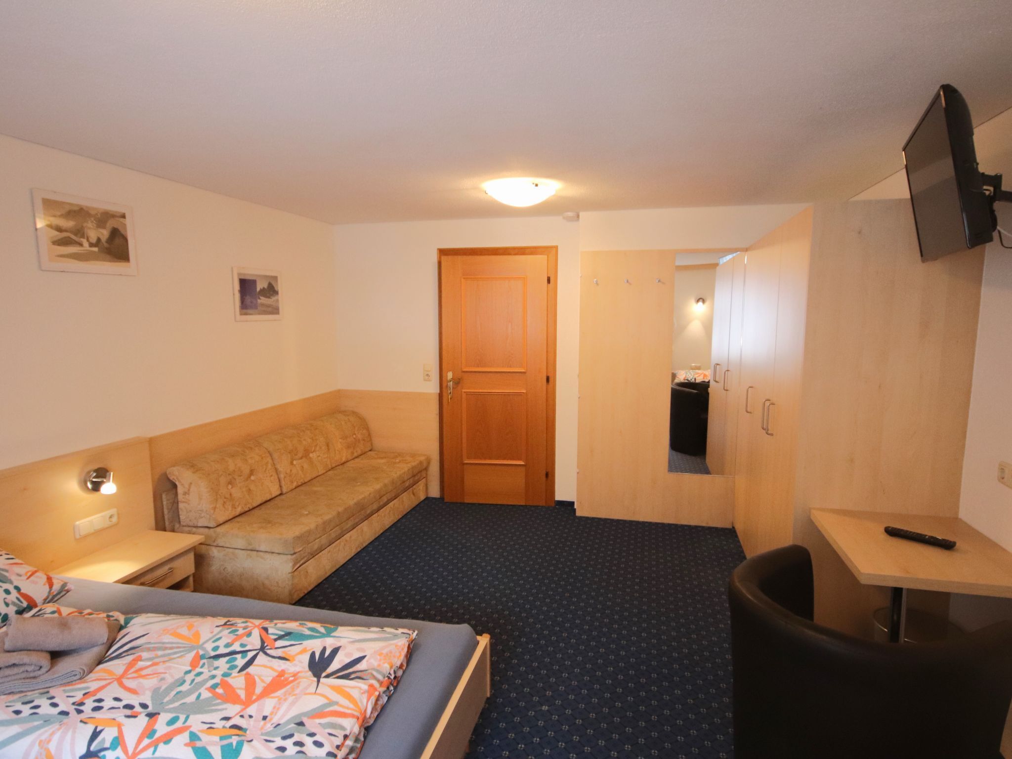 A hotel room with a bed, a sofa, a desk, and a TV.