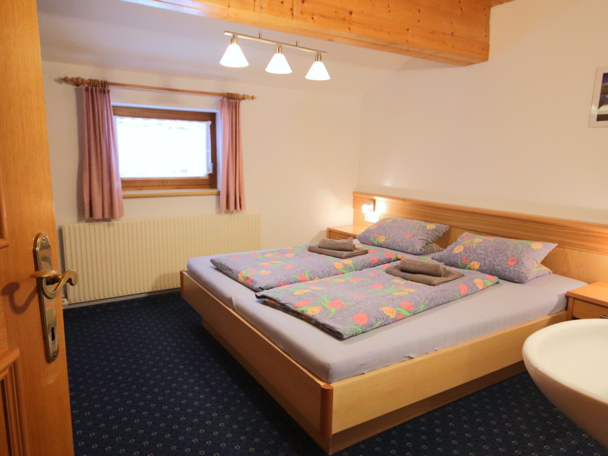 A bedroom with a wooden bed, two bedside tables, a window with curtains, and a radiator.