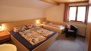 Una habitación con techo de madera, una cama con ropa de cama floral, una silla y un ventanal con cortinas.