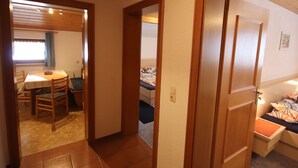 Una habitación con techo de madera, comedor con mesa y sillas, y cama con colcha colorida.
