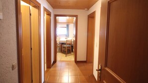 Un pasillo con puertas de madera y piso de baldosas que conduce a un comedor con mesa y sillas.