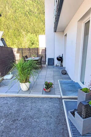Une terrasse avec une table et des chaises, un barbecue et des plantes en pot.