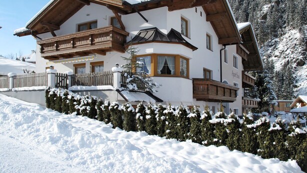 Un grand chalet à plusieurs étages, doté d’une façade en bois, d’un balcon et surplombant un paysage enneigé.