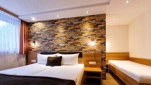 Une chambre d’hôtel avec un grand lit, un lit plus petit, une table de chevet et un mur orné d’un motif texturé.
