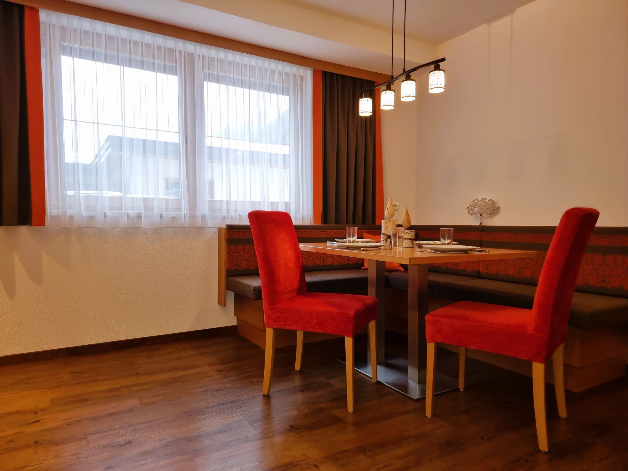 A dining area with a wooden table, red upholstered chairs, and a modern pendant light.