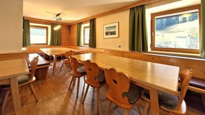 Un comedor con mesas y sillas de madera, ventanas grandes con cortinas y una lámpara en el techo.