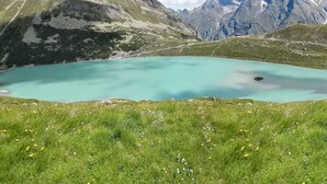 Paisaje de montaña con un lago turquesa rodeado de praderas y montañas rocosas.