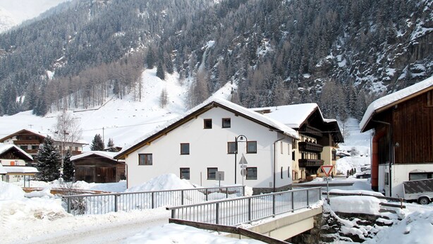 Un pueblo cubierto de nieve con casas de madera tradicionales, un puente y montañas al fondo.