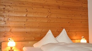 Una habitación con paneles de madera, una cama, dos almohadas y una mesita de noche con una lámpara.