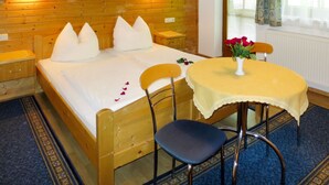 A wooden bed with white pillows, a bedside table, a chair, a small table with a vase of flowers, and a window with curtains. - Landhaus Heim by Interhome (Zell am Ziller)