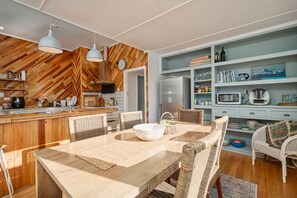 Une cuisine moderne agrémentée d'éléments en bois, un coin repas avec des meubles en osier, et une étagère bleu clair où sont disposés divers objets.