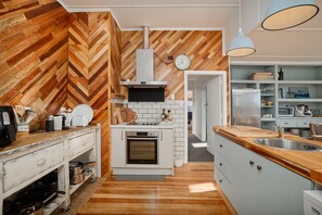 Une cuisine avec un mur en bois à motifs en chevrons, un four encastré, des armoires blanches et un plan de travail en bois.