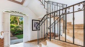 Una escalera con barandillas de metal decoradas y vista a un jardín a través de una puerta abierta.
