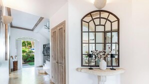 Un pasillo con un espejo arqueado grande, un banco de piedra y una puerta que da a un jardín.