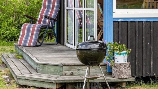A wooden deck with two striped lawn chairs, a black grill, and a potted plant. - Enerhögen Flädern by Interhome (Bullaren)