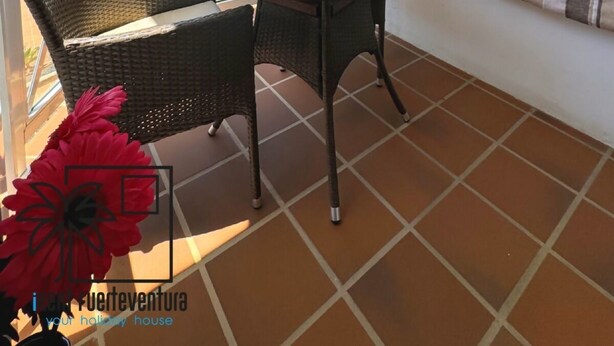 Un balcón con una mesa de vidrio y sillas de mimbre, un sofá blanco con cojines y vistas a una piscina.