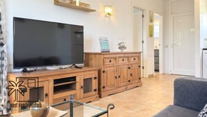 Una sala de estar con televisión de pantalla plana, muebles de madera, una mesa de centro de vidrio y un sofá gris.