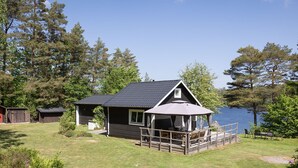 Eine Hütte mit einer Terrasse mit Blick auf einen See, umgeben von Bäumen.