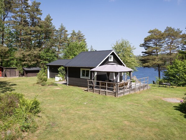 A cabin with a deck overlooking a lake, surrounded by trees.