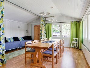 A cozy room with a wooden dining table, chairs, a sofa, and a window with green curtains.
