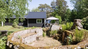 Eine rustikale Holzhütte mit dunklem Dach, einer kleinen Veranda und einem Steingebilde im Vordergrund.