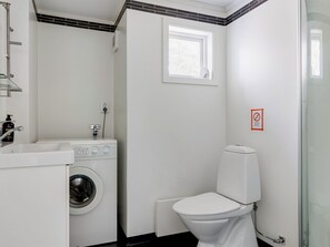 A compact, modern bathroom with a washing machine, a toilet, and a small window providing natural light.