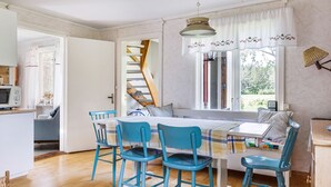 Una habitación acogedora con una mesa de comedor, cuatro sillas azules, una escalera, un ventanal con cortinas y una lámpara colgante.