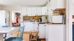 Una cocina compacta con armarios blancos, una encimera de madera y un área de comedor con una silla y una mesa azules.