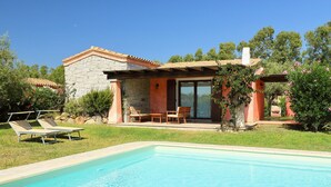 A poolside area with a stone building, a pool, and a patio with chairs. - Ville San Pietro (REI355) by Interhome (Costa Rei)