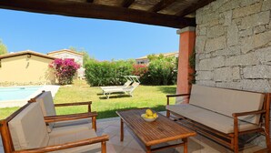 An outdoor patio with a wooden table, two cushioned chairs, and a stone wall. - Ville San Pietro (REI355) by Interhome (Costa Rei)