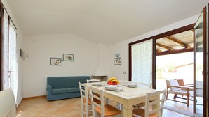 A dining area with a table set for four, a blue sofa, and a glass door leading outside. - Ville San Pietro (REI355) by Interhome (Costa Rei)