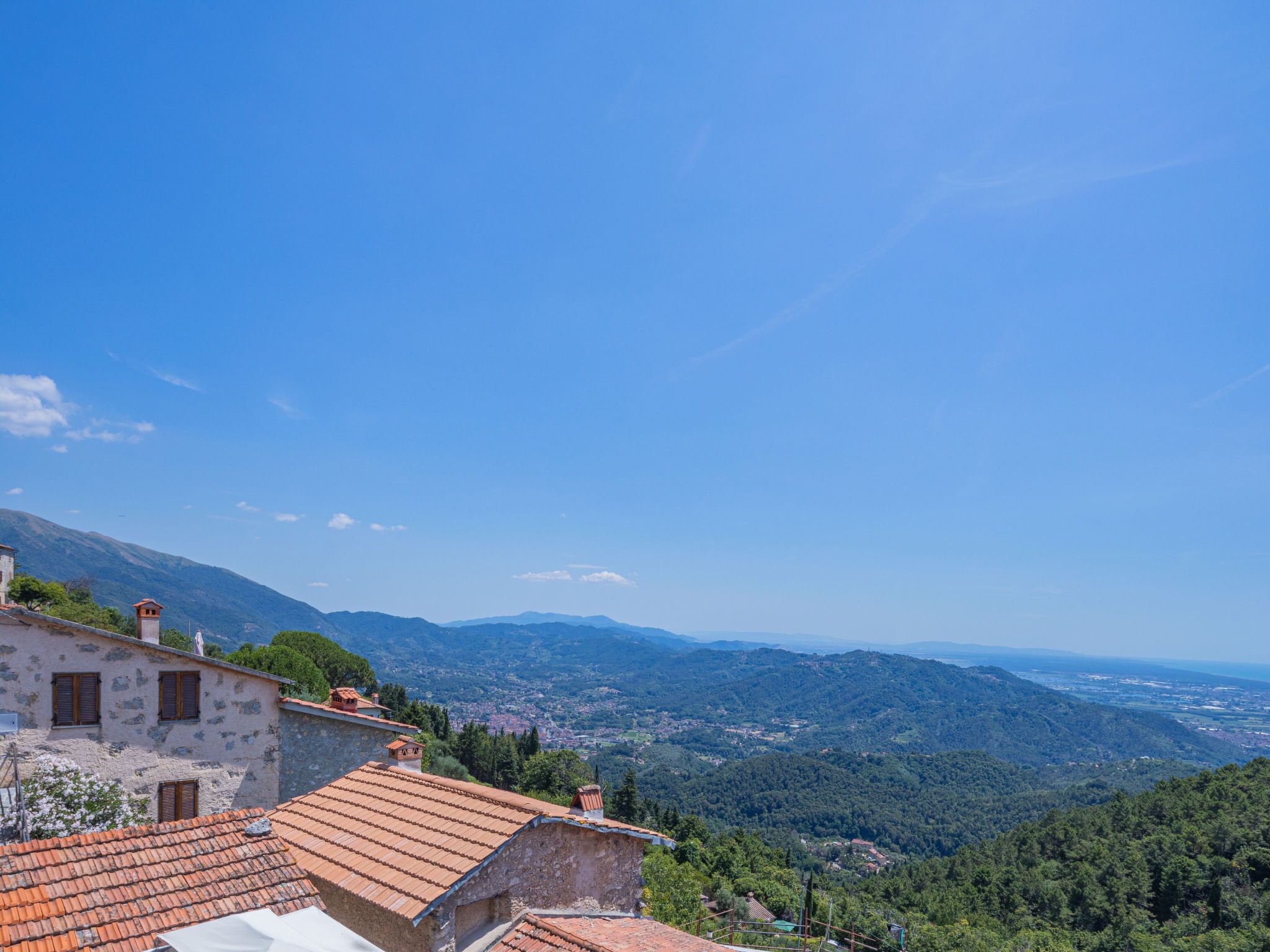 A hillside village with terracotta-roofed buildings, a clear blue sky, and a view of distant mountains.