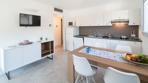 A modern kitchen with white cabinets, a flat-screen TV, and a dining area with a wooden table and white chairs. - Torre Bianca by Interhome (Lignano Sabbiadoro)