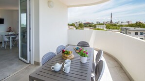 A balcony with a table set for two, a potted plant, and a view of the cityscape. - Torre Bianca by Interhome (Lignano Sabbiadoro)