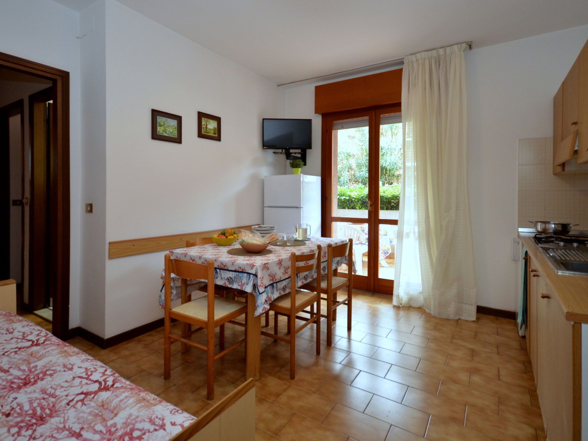A dining area with a table set for four, a television on the wall, and a kitchen area with a stove.