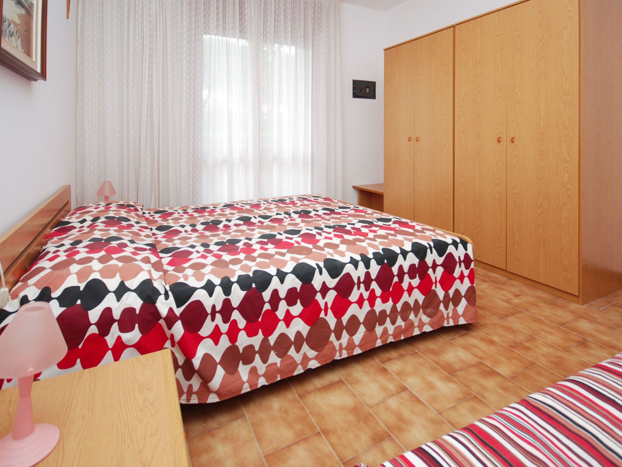 Une chambre à coucher avec un lit, une armoire en bois, une table de chevet et une fenêtre ornée de rideaux légers.
