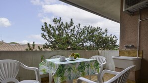 A balcony with a table covered in a floral tablecloth, surrounded by white plastic chairs.