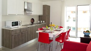 A modern kitchen with white cabinets, a microwave, and a dining area with red chairs and a white table. - Residence Monica by Interhome (Lignano Sabbiadoro)