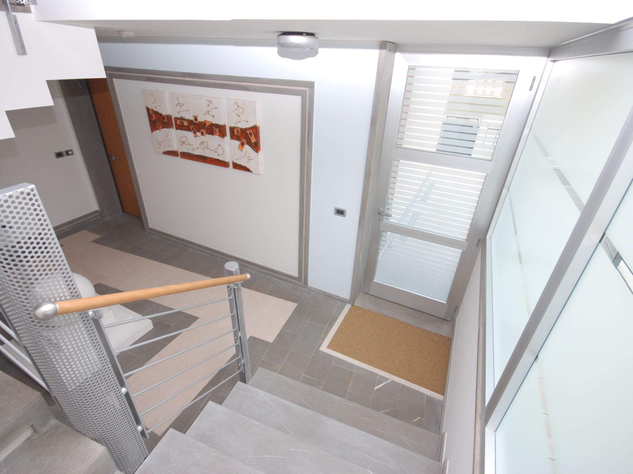 A modern interior with a staircase, a door with a poster, and a window with blinds.